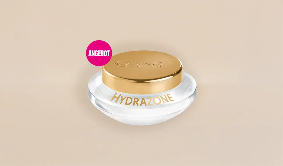 Tiegel Guinot Hydrazone vor beige­farbenem Hintergrund, mit pinkem Kreis und weißer Aufschrift ‚Angebot‘ oben links.